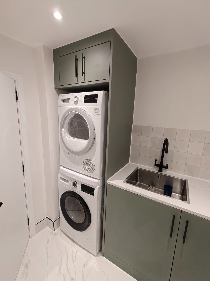 Utility room with green cabinetry, sink and stacked laundry